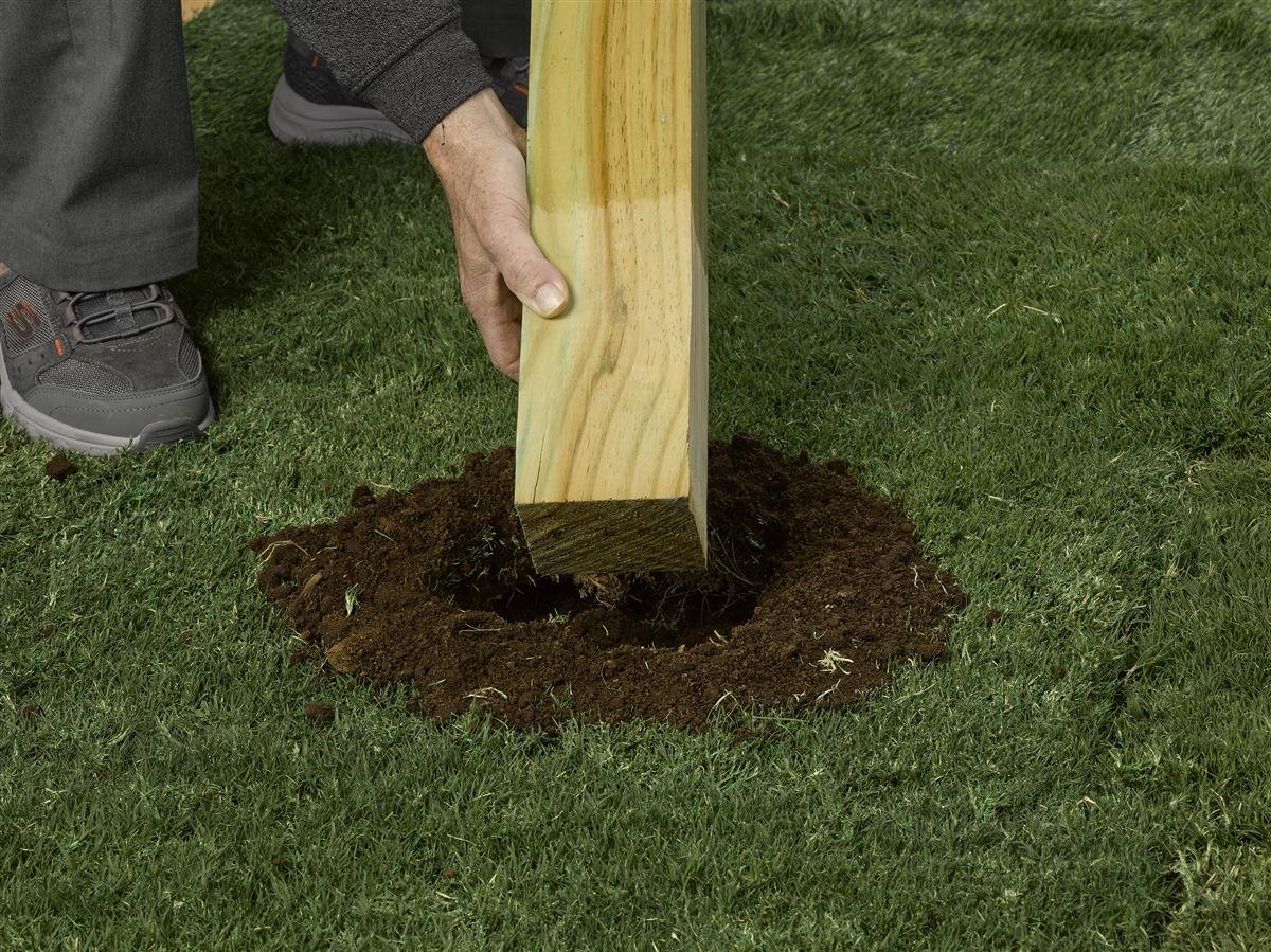 A coated deck post being set into the ground, the ground-contact end sealed against moisture before backfilling